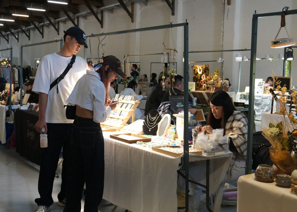 活動花絮：一對情侶在市集飾品攤位前低頭挑選耳環與項鍊，攤主坐在桌後整理商品
